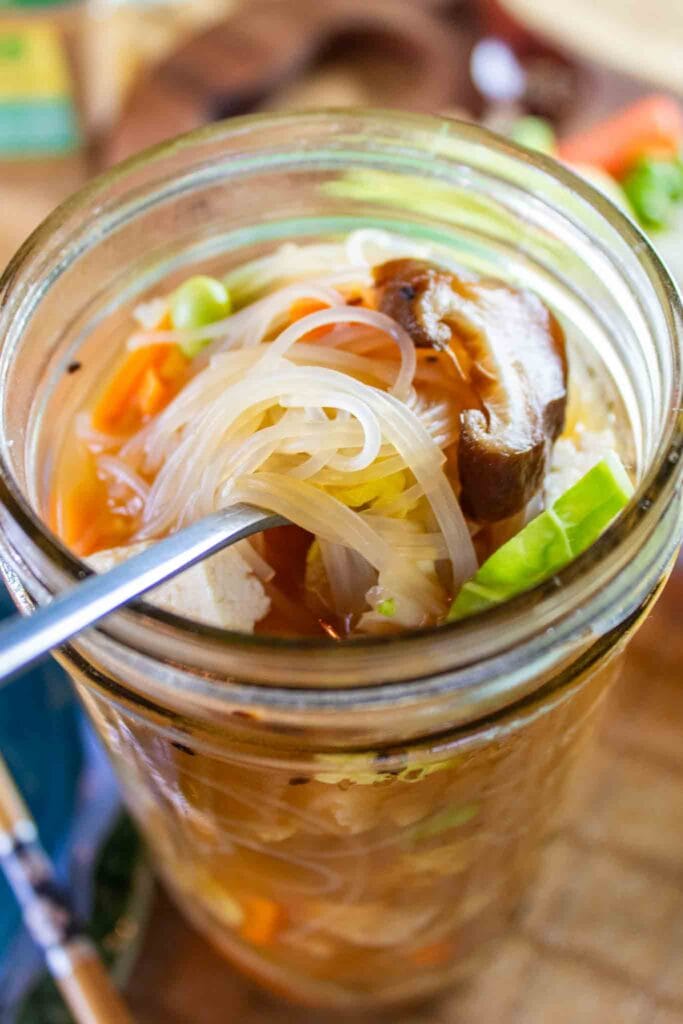 asian mason jar soup with a fork lifting the noodles up out of the broth.