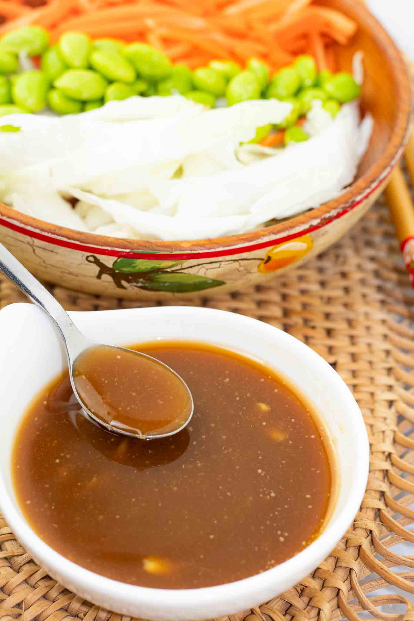 white bowl of vegan miso dressing with a spoon dipping and salad in the background.