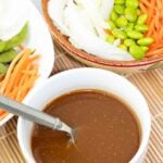white bowl filled with homemade miso dressing and a spoon with vegetables in bowls around it.