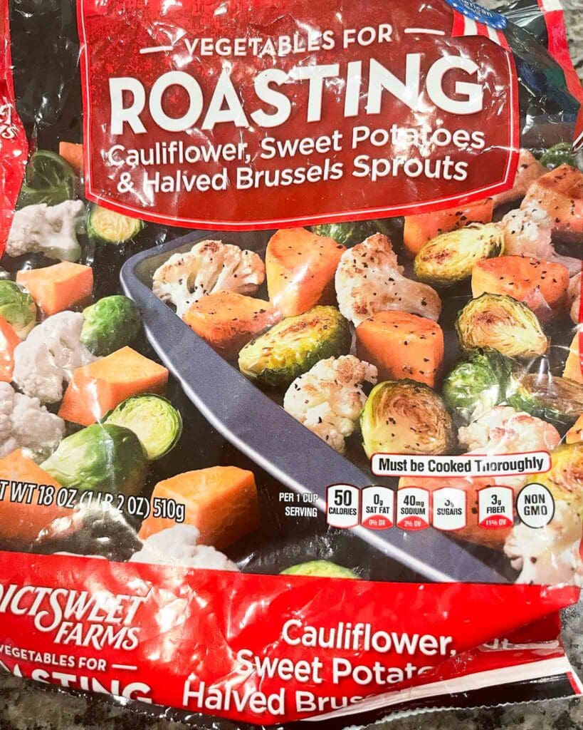 roasting vegetables in a red back from trader joes that include cauliflower, sweet potatoes, and brussels sprouts.