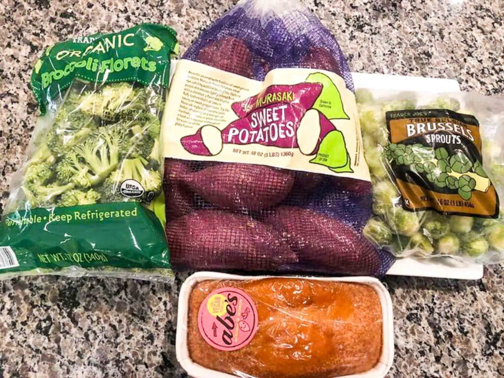 purple sweet potatoes, broccoli florets, and brussels sprouts from trader joes on a counter top.