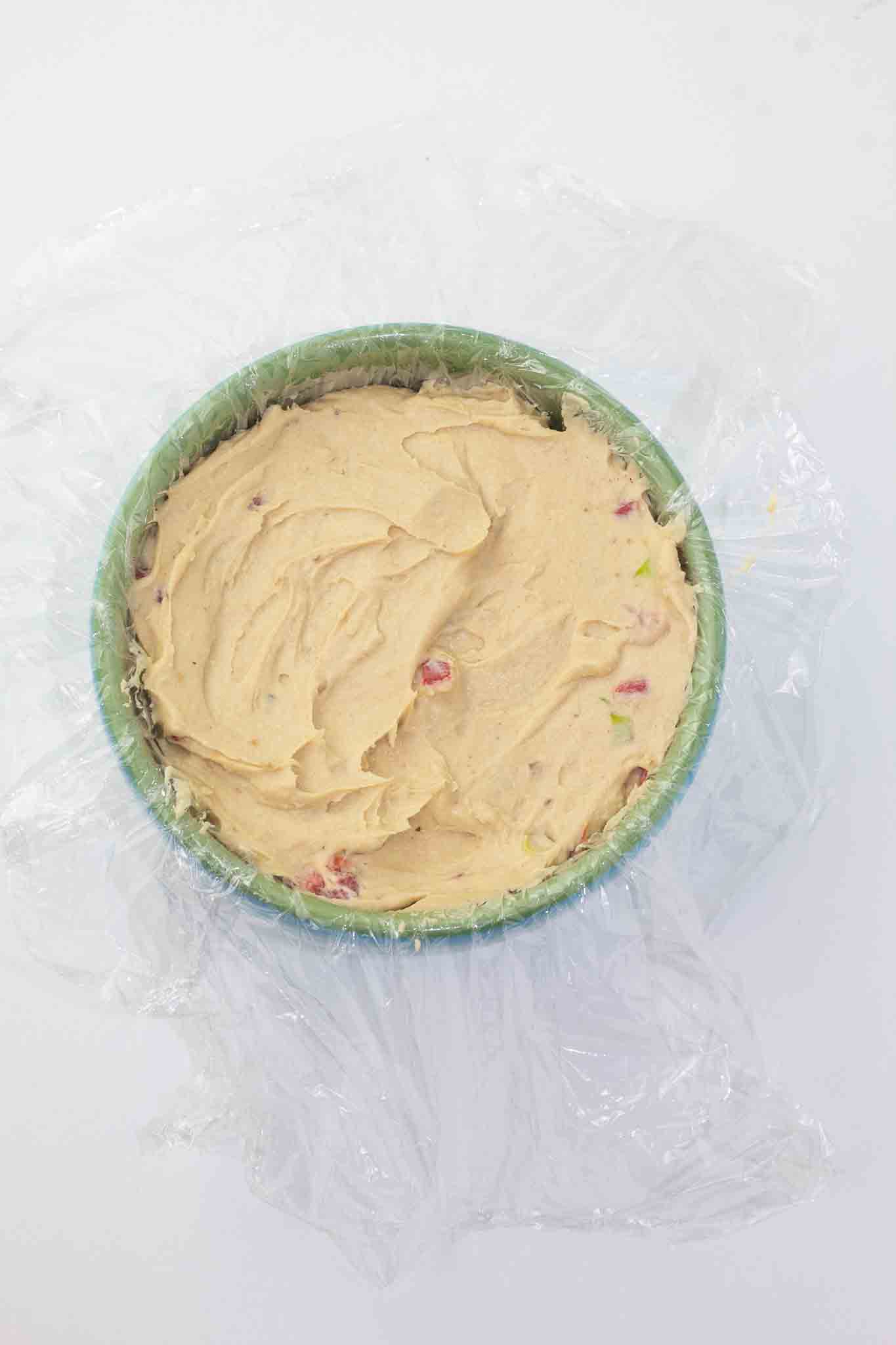 small bowl lined with plastic wrap with a dairy-free cheese ball mixture poured in ready to be chilled in the refrigerator.