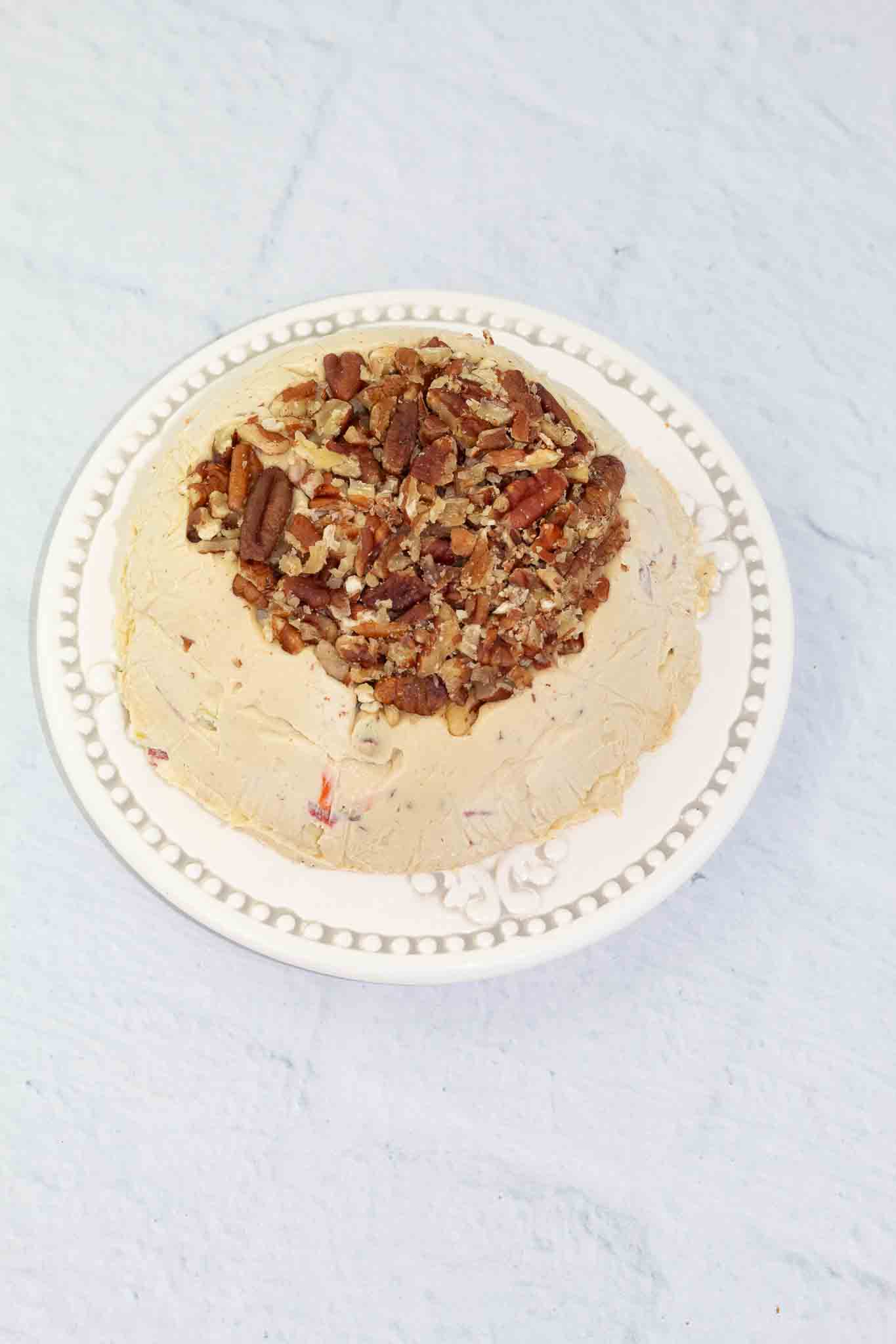 white plate with a vegan cheese ball topped with pecan pieces after being chilled and dumped out of bowl.