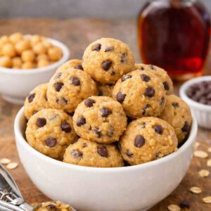 edible cookie dough balls in a white bowl with a cookie scoop beside it.