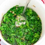 large red and white stockpot with braised kale and stainless spoon.