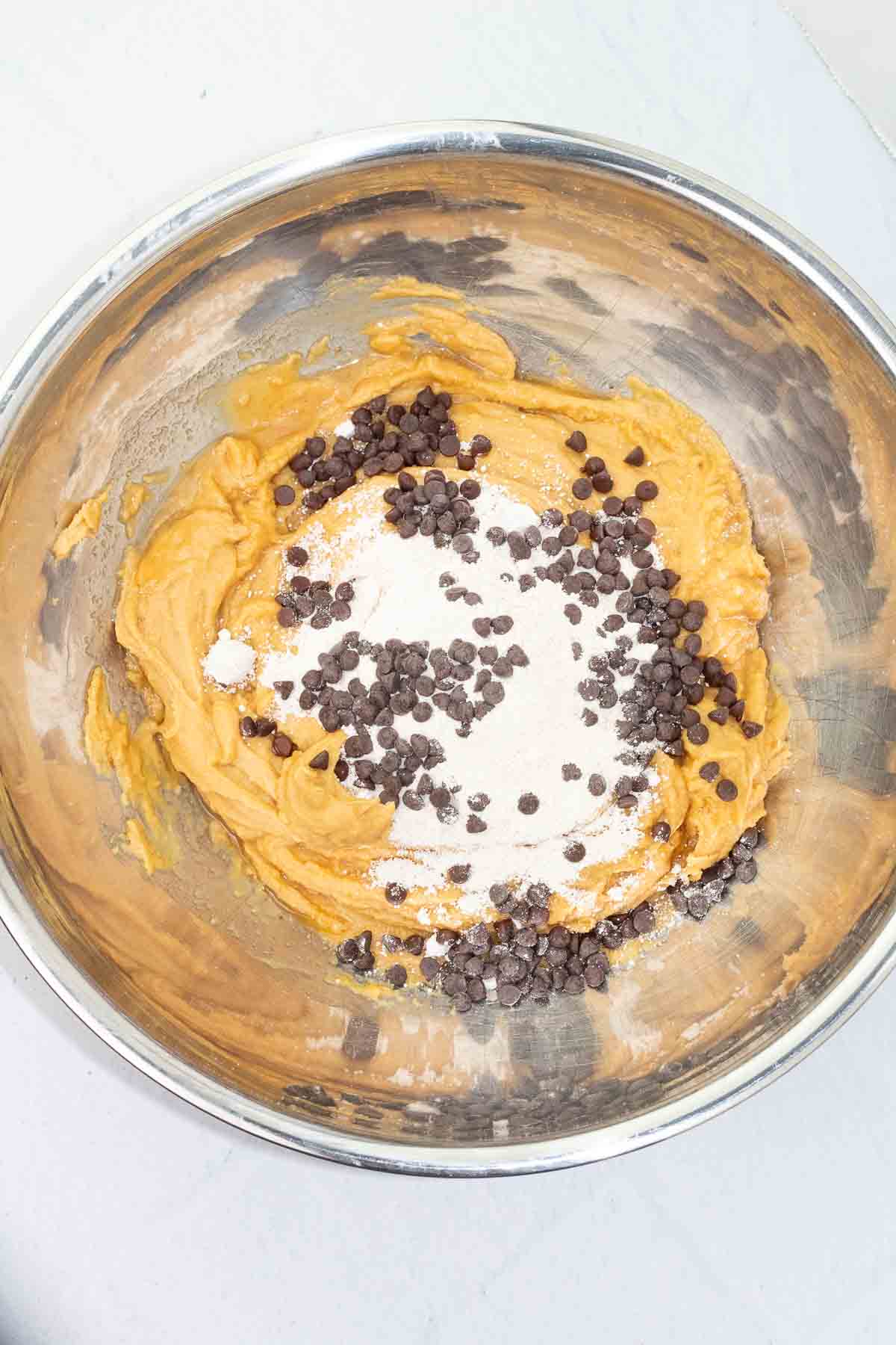 stainless mixing bowl filled with vegan cookie dough, oat flour, and chocolate chips.