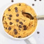 white coffee muf full of homemade vegan cookie dough batter with a spoon and sprinkled with vegan chocolate chips.
