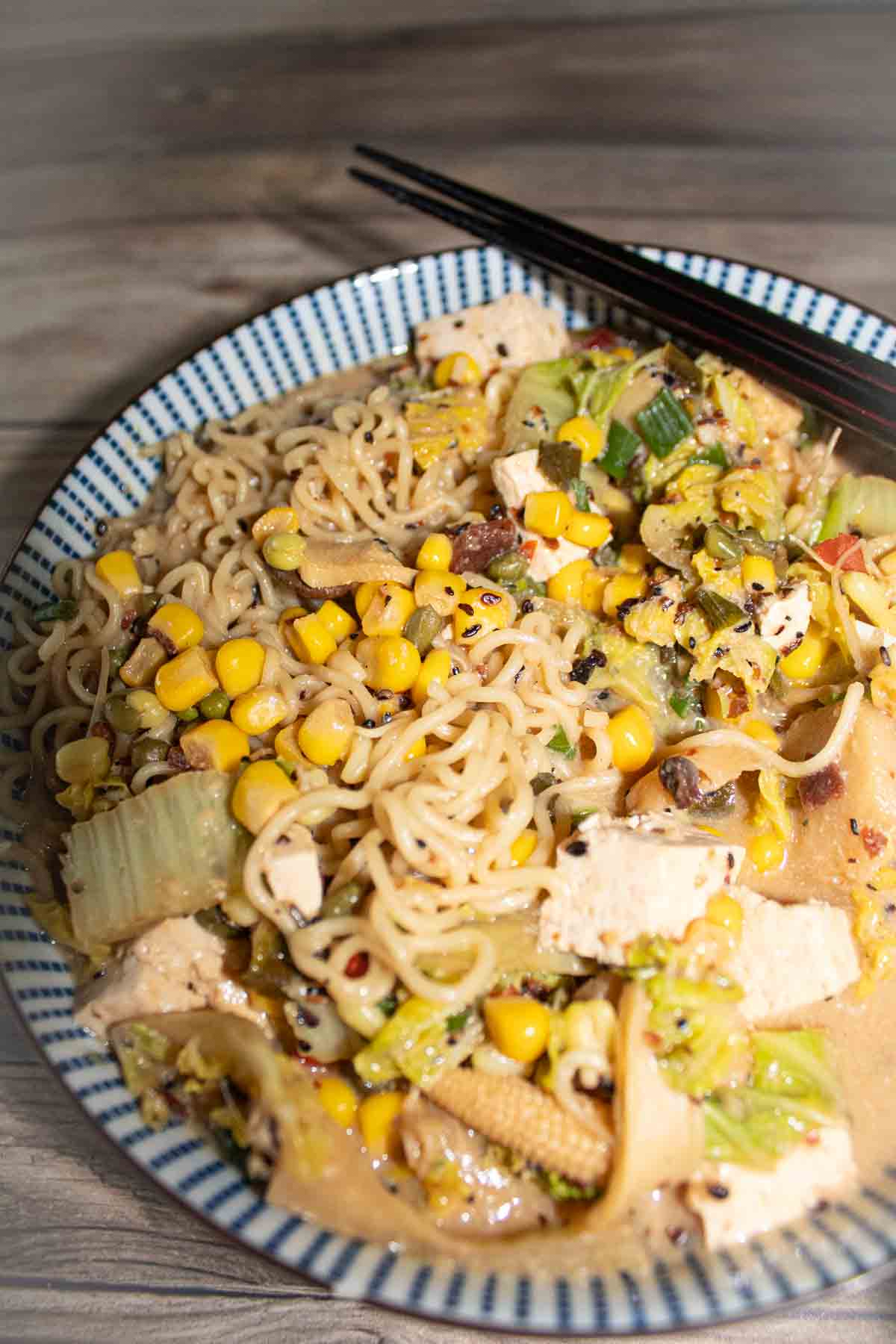 blue and white striped asian bowl filled with miso ramen noodles and vegetables with black chopsticks.