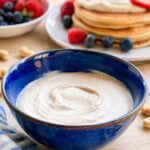 vanilla cashew cream in a blue bowl with pancakes and fruit in background.