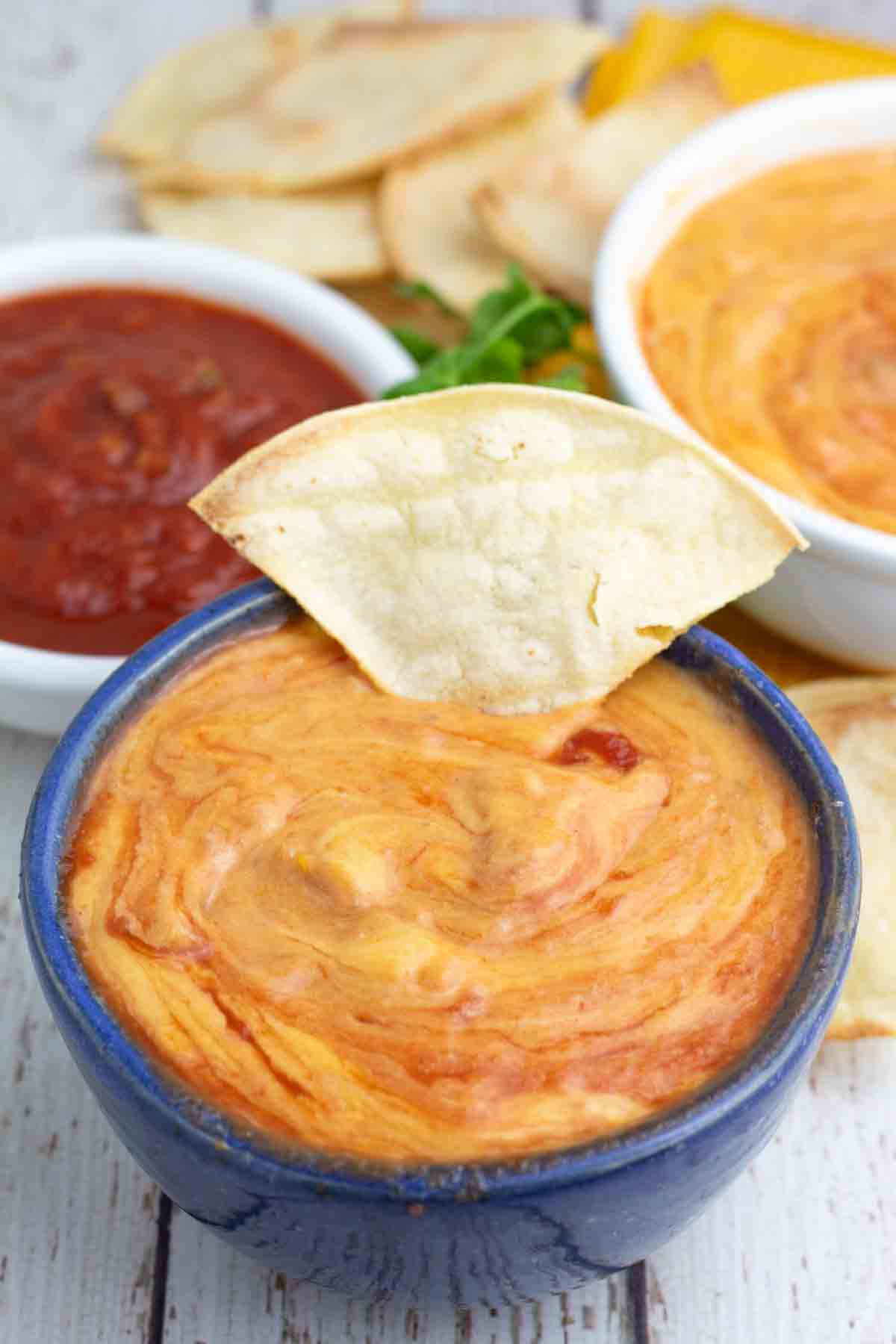 blue bowl of vegan nacho cheese with a homemade tortilla chip being dipped in it.