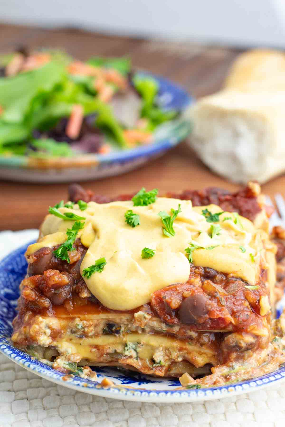 big serving of spinach lasagna dripping with vegan homemade cheese sauce on a bright blue plate.