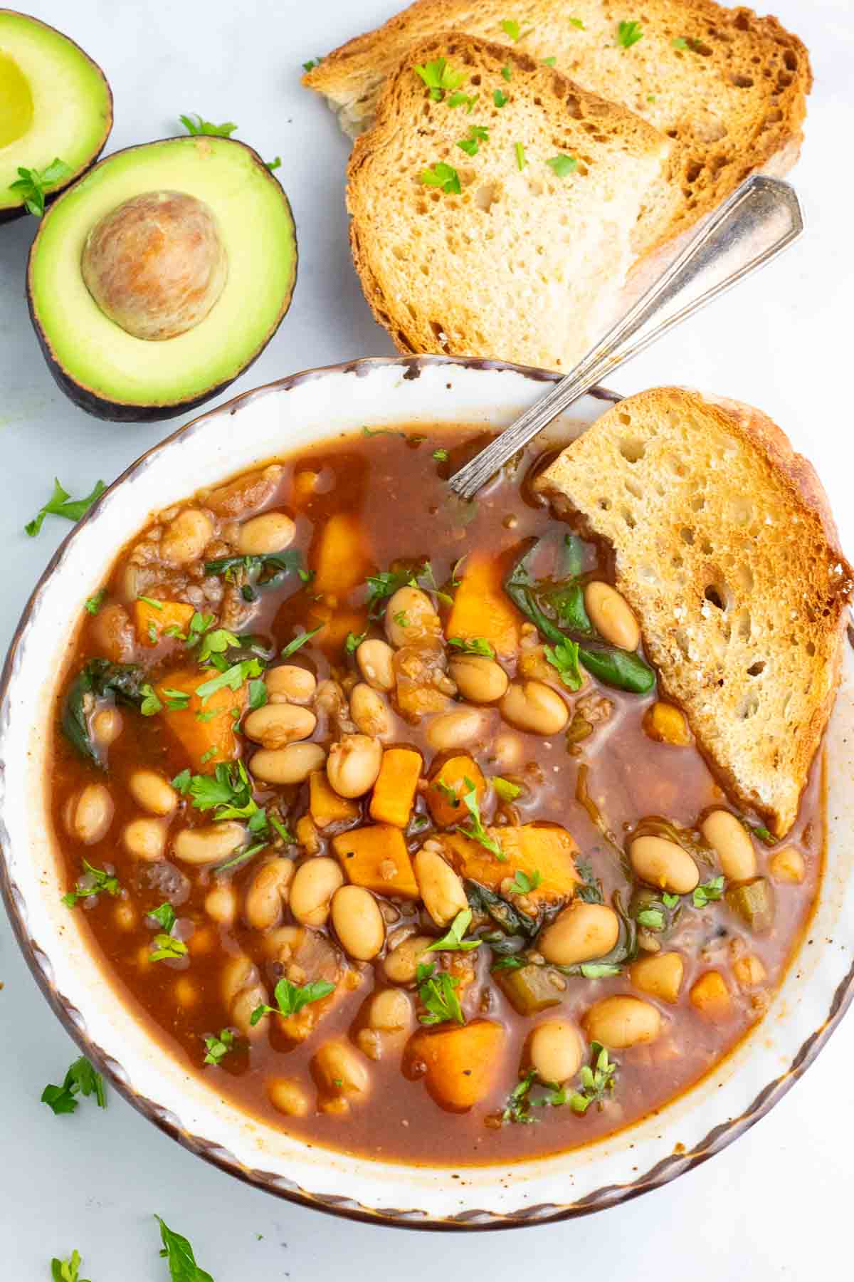 white bean soup in a bowl with toasted sour dough bread and sliced avocado.