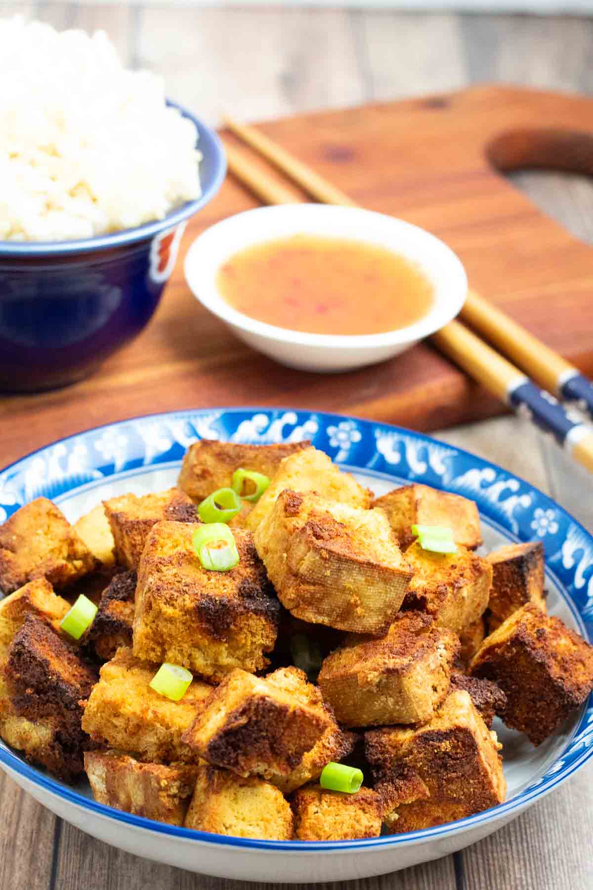 cubes of crispy air fried tofu in a bright blue dish with chopsticks and small white dish of sweet and sour sauce in background.