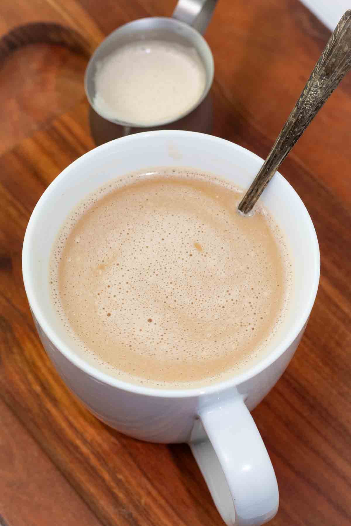 white coffee cup filled with coffee and thick vegan creamer wiht a long handle spoon sticking out.