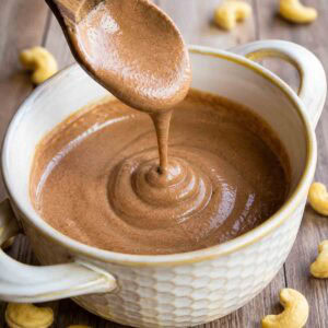drizzle shot of chocolate cashew cream in a bowl with a wooden spoon.