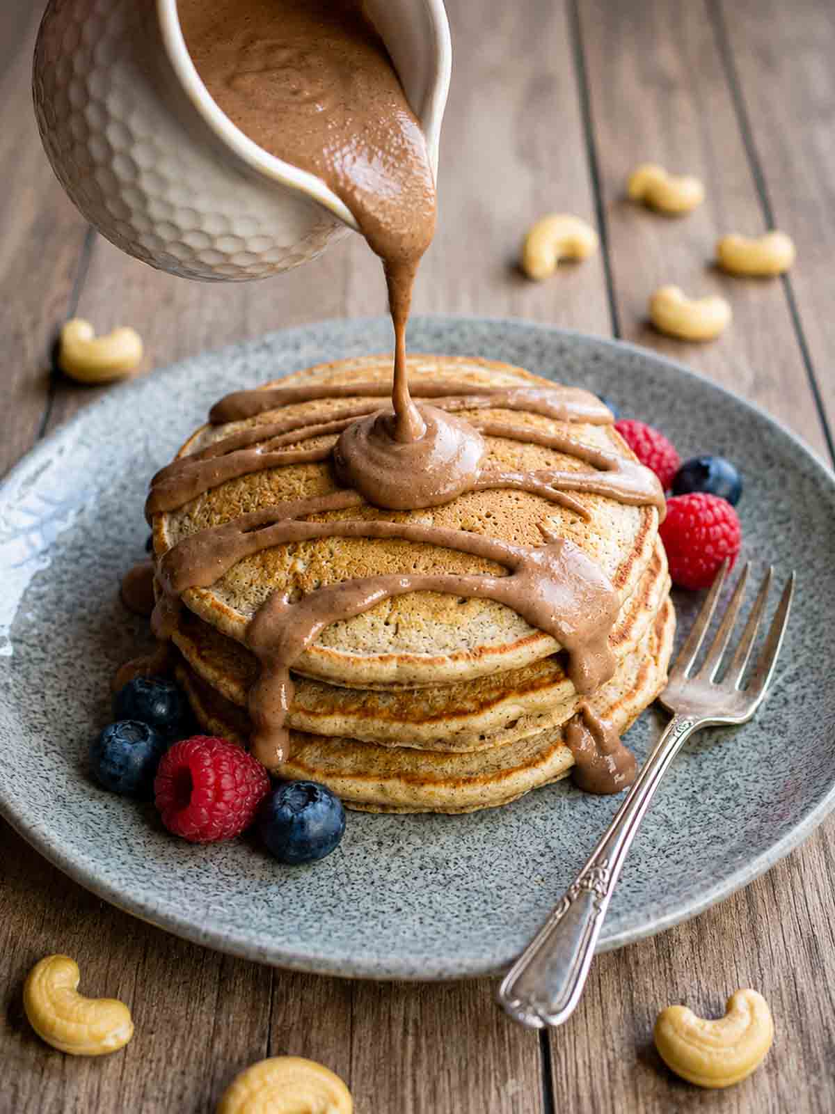 pancakes with chocolate cashew cream being poured over the top.