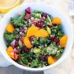 white bowl of kale quinoa salad and topped with madarin orange slices.