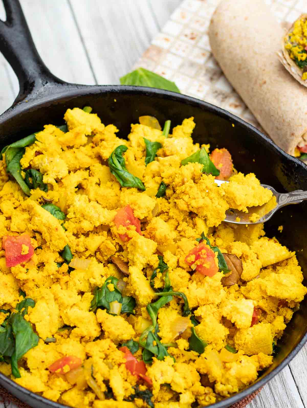 black cast iron skillet filled with tofu breakfast scramble with veggies.