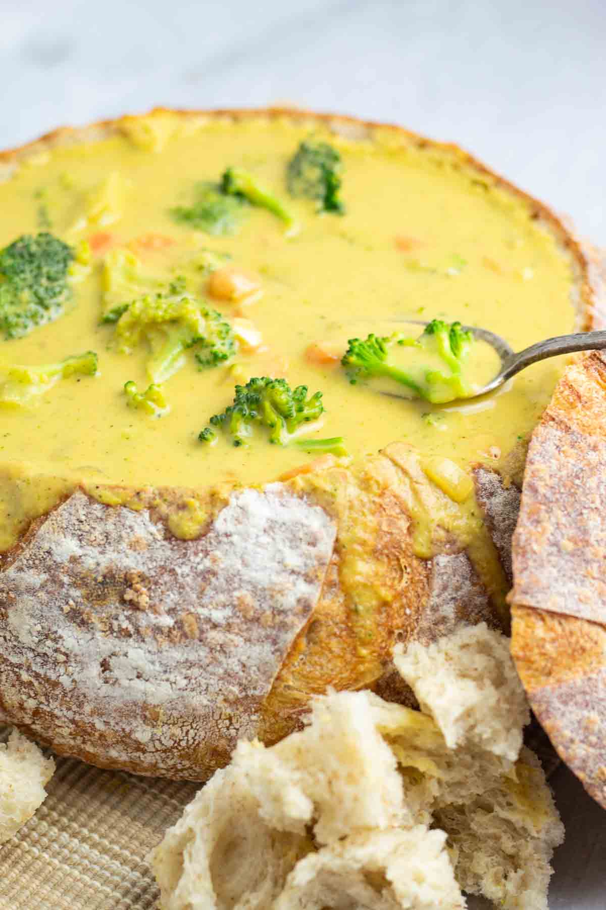 sourdough soup bowl filled with vegan broccoli cheddar soup with a spoon and chunks of bread around it.