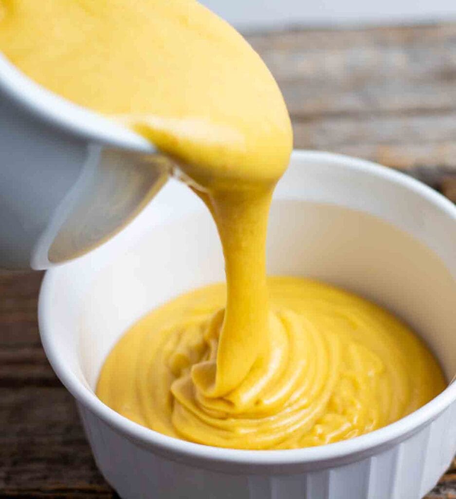 vegan cheese sauce being poured into a white bowl.