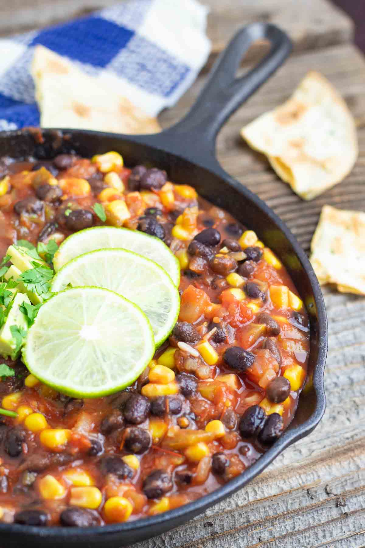 cast iron black pan filled with black bean corn vegan chili topped with lime slices and fresh cilantro.