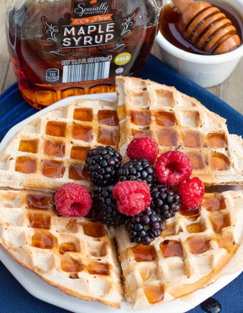 white plate with large gluten-free waffle made from oat flour and topped with maple syrup and berries.
