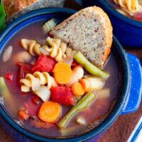 bright blue bowl filled with vegan minestrone soup with a slice of crusty bread in the bowl.