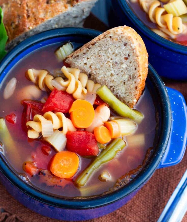 bright blue bowl filled with vegan minestrone soup with a slice of crusty bread in the bowl.