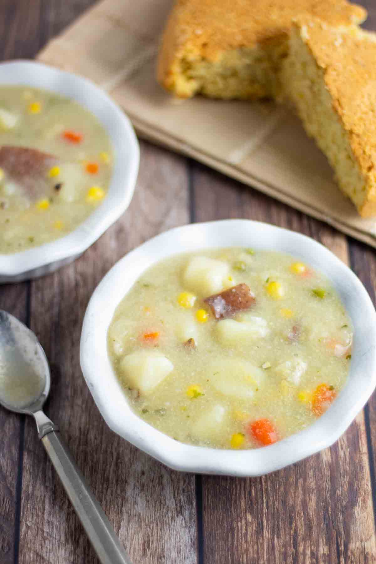 2 white bowls filled with vegan potato soup with slices of cornbread in the background.