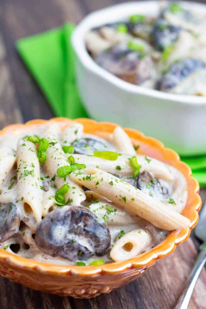 bright orange bowl filled with vegan mushroom stroganoff on a wooden table.