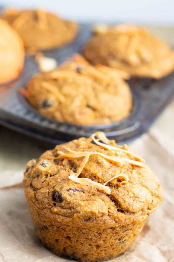 one sweet potato muffin up close and a muffin pan filled with muffins in the background.