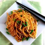 white square plate filled with ginger soba noodles and topped with chives and black chopsticks on side of plate.