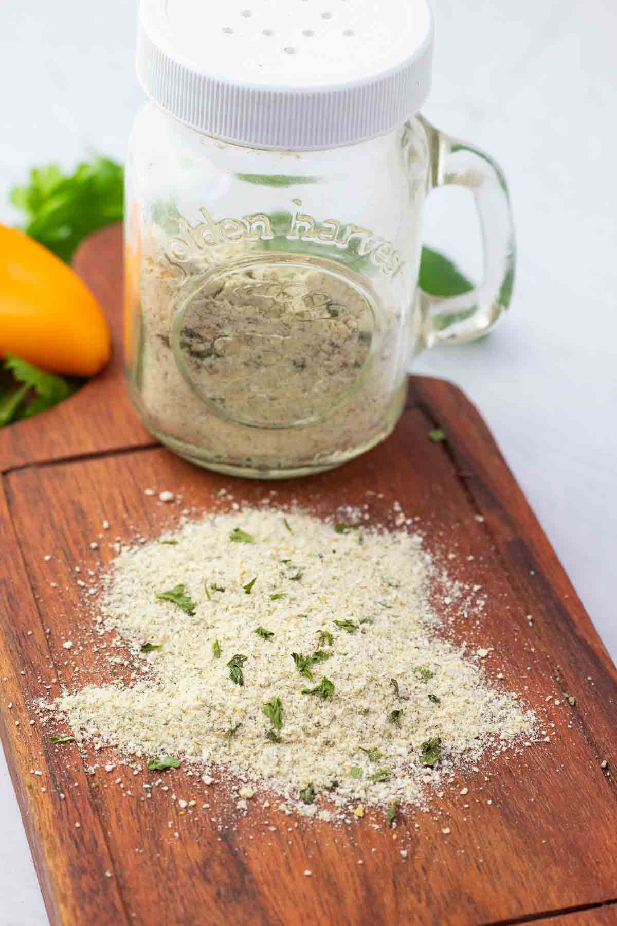 glass shaker bottle filled with dairy-free ranch seasoning on a wooden board with some sprinkled on the board.