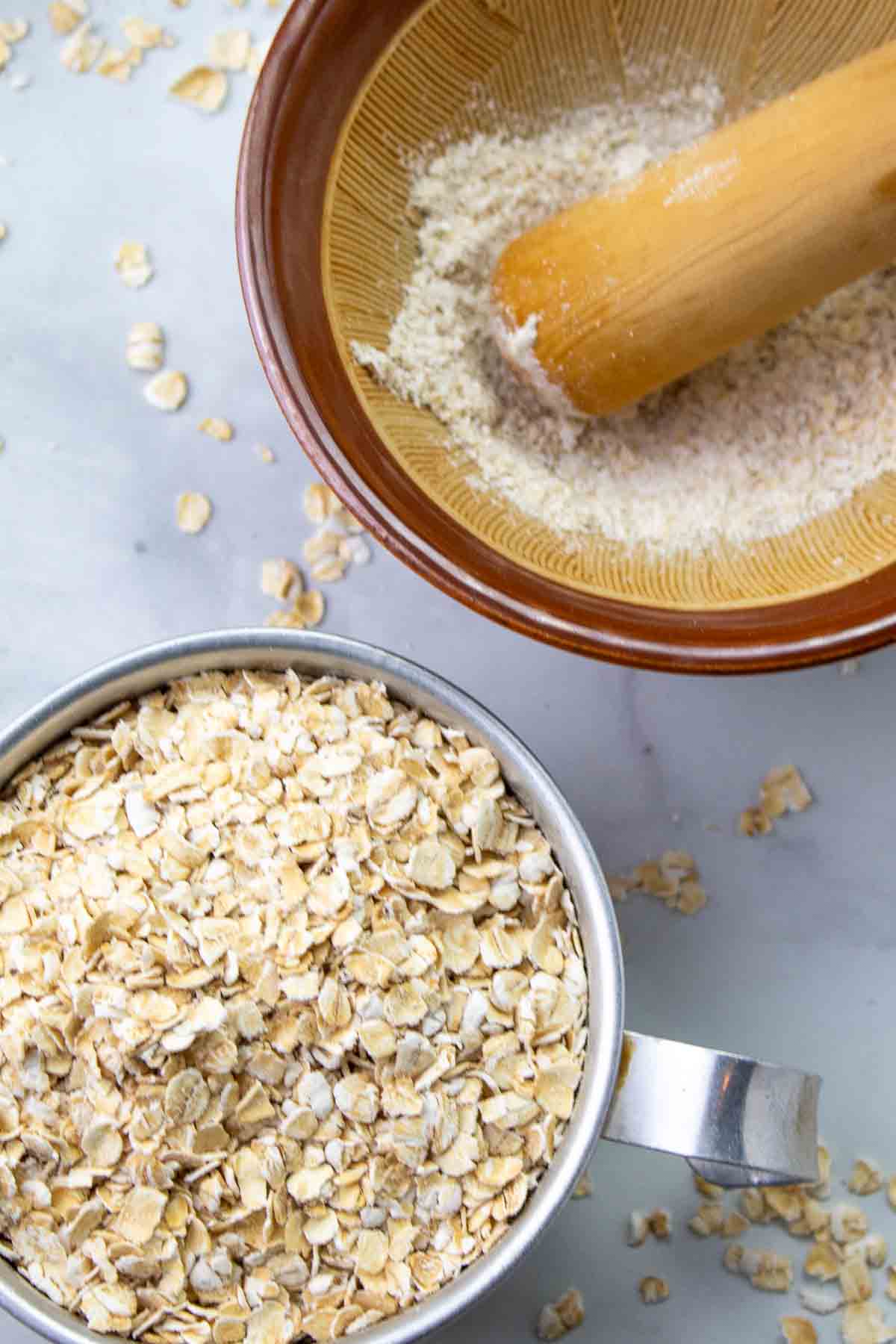 metal measuring cup filled with oats and a bowl with mortar and pestle grinding it.