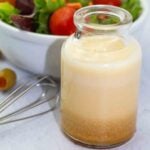 small clear jar filled with homemade miso sauce with a bowl of green mixed salad in the background.