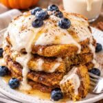 stack of vegan pumpkin pancakes topped with cashew cream sauce and blueberries.