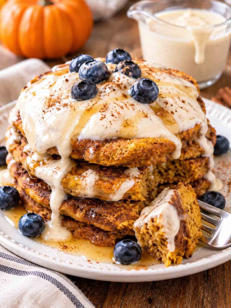 stack of vegan pumpkin pancakes topped with cashew cream sauce and blueberries.