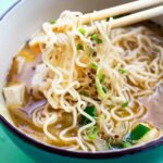 bright green bowl filled with ramen noodles being picked up with chopsticks.