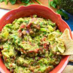 colorful orange bowl full of chunky guacamole with a tortilla chip for dipping.