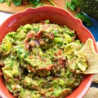 colorful orange bowl full of chunky guacamole with a tortilla chip for dipping.