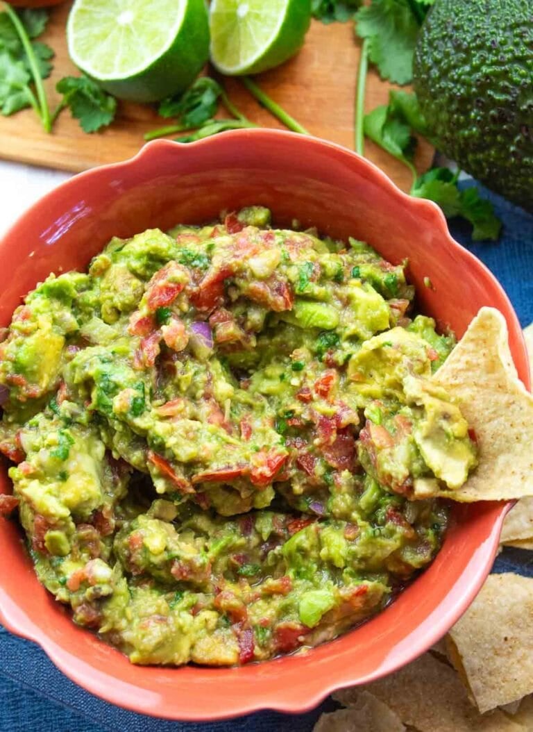 colorful orange bowl full of chunky guacamole with a tortilla chip for dipping.