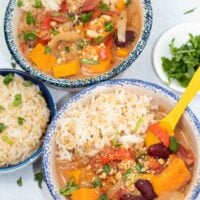 2 bowls of african sweet potato stew in blue crock bowls with colorful yellow soup spoons.