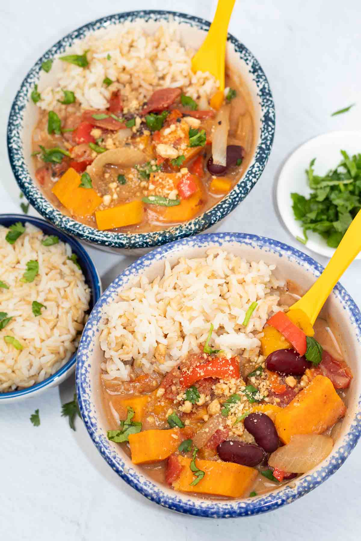 2 bowls of african sweet potato stew in blue crock bowls with colorful yellow soup spoons.