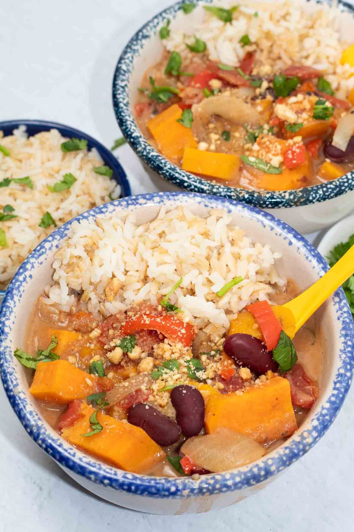 close up of african sweet potato stew in a decorative bowl with beans, red bell peppers, and crushed peanuts.
