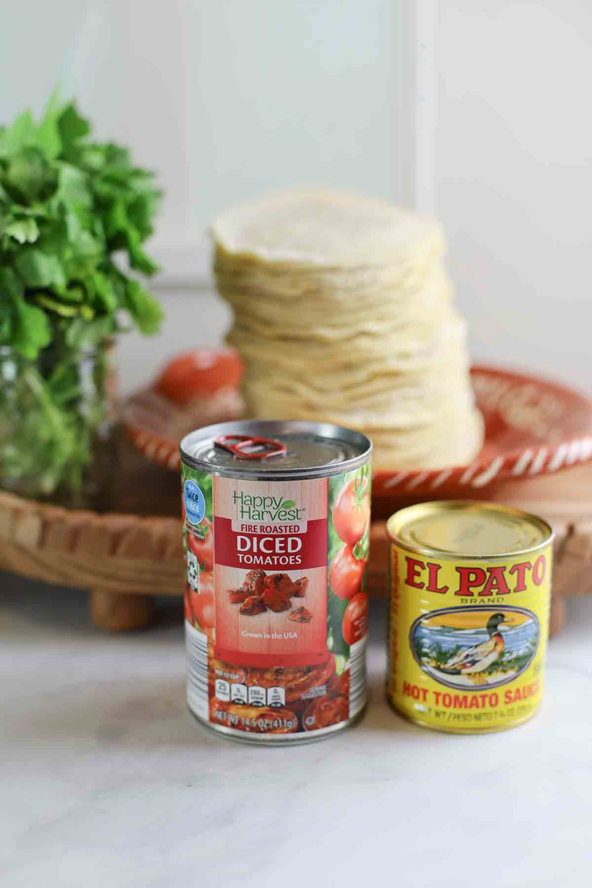 can of diced fire-roasted tomatoes and can of elpato hot tomato sauce with corn tortillas stacked in background.