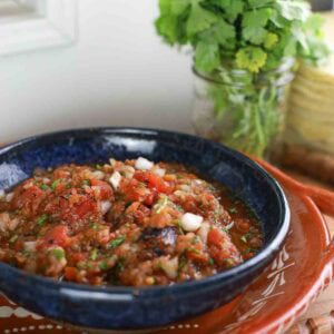 big blue bowl full of homemade red salsa with jar of cilantro in background.