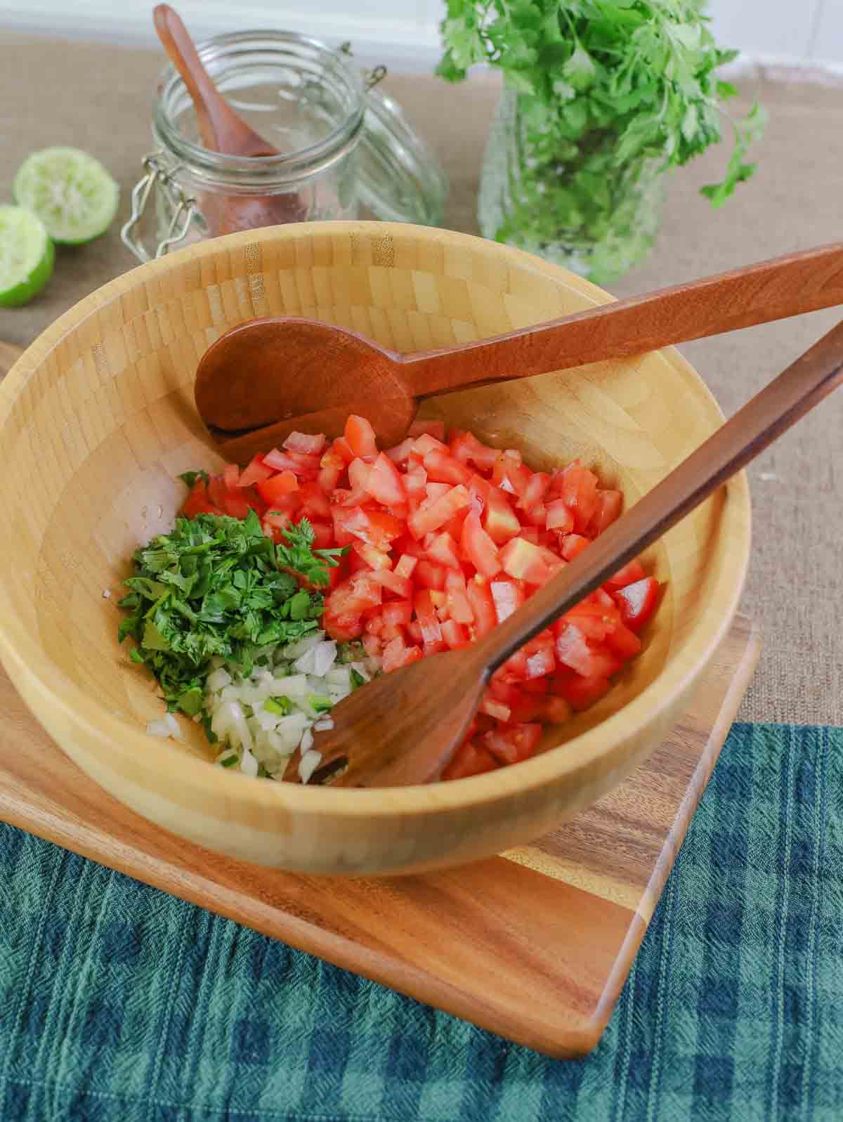 wooden bowl with diced jlapeno, chopped onion, cilantro, and tomatoes with spoon and fork for mixing.