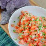 white bowl filled with colorful fresh pico de gallo on a wooden board.