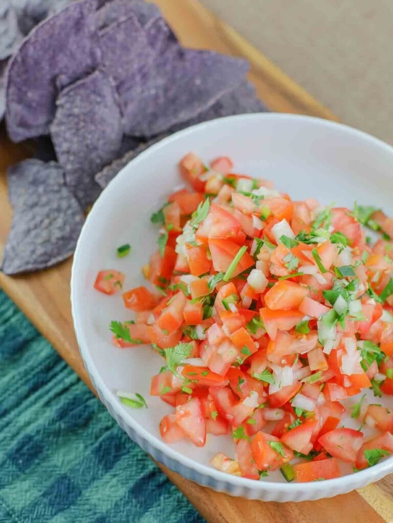 white bowl filled with colorful fresh pico de gallo on a wooden board.