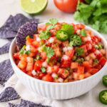 white bowl of pico de gallo topped with cilantro and blue chips.